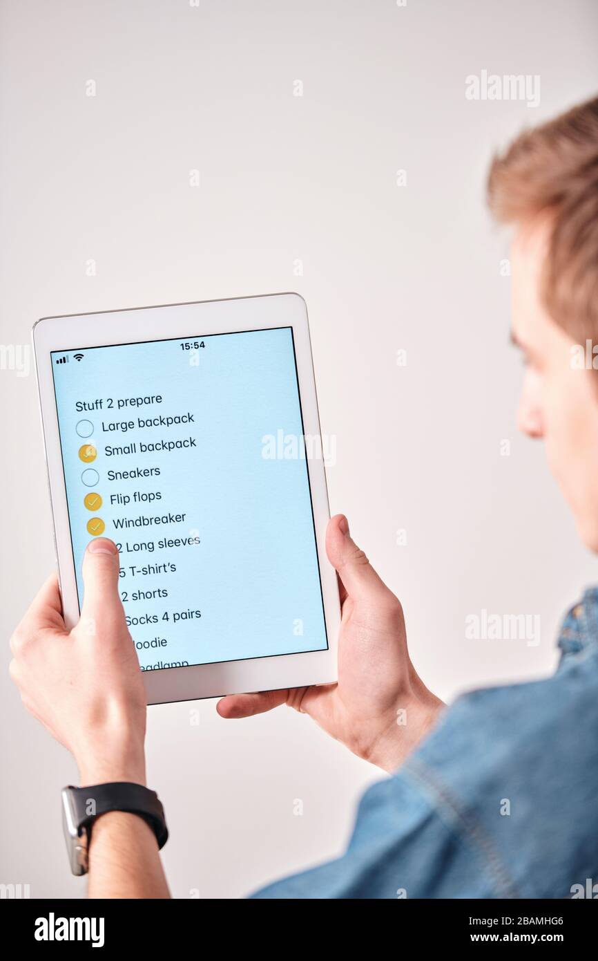 Vista a spalla del giovane uomo che usa la lista di imballaggio nella nota del tablet mentre mette il segno di spunta in roba imballato Foto Stock