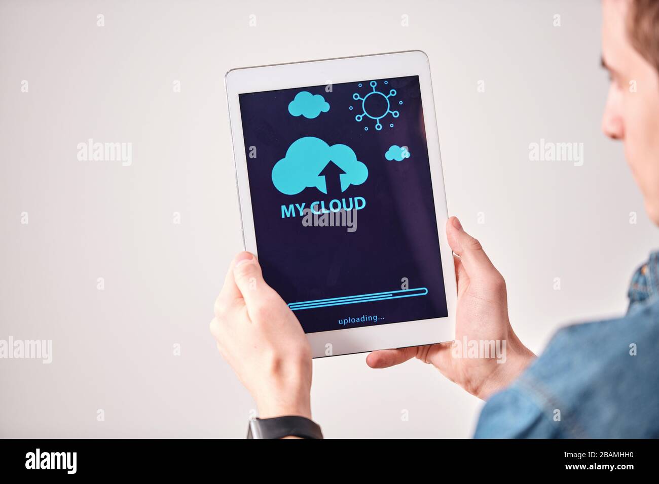 Vista a spalla di un giovane che utilizza un tablet digitale durante il caricamento di file sul servizio cloud Foto Stock