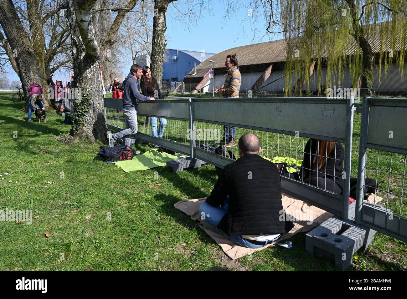 Konstanz, Germania. 26 marzo 2020. Diverse coppie stanno chiacchierando sul confine tedesco-svizzero tra Costanza e Kreuzlingen. Le coppie sono separate da un recinto di confine e questo è l'unico modo per abbracciare e incontrare. Decine di coppie e famiglie si sono incontrate per vedersi al confine lungo diverse centinaia di metri, normalmente aperto a pedoni e ciclisti. La polizia svizzera e un servizio di sicurezza controllano la distanza tra le coppie e le famiglie. Credit: Felix Kästle/dpa/Alamy Live News Foto Stock