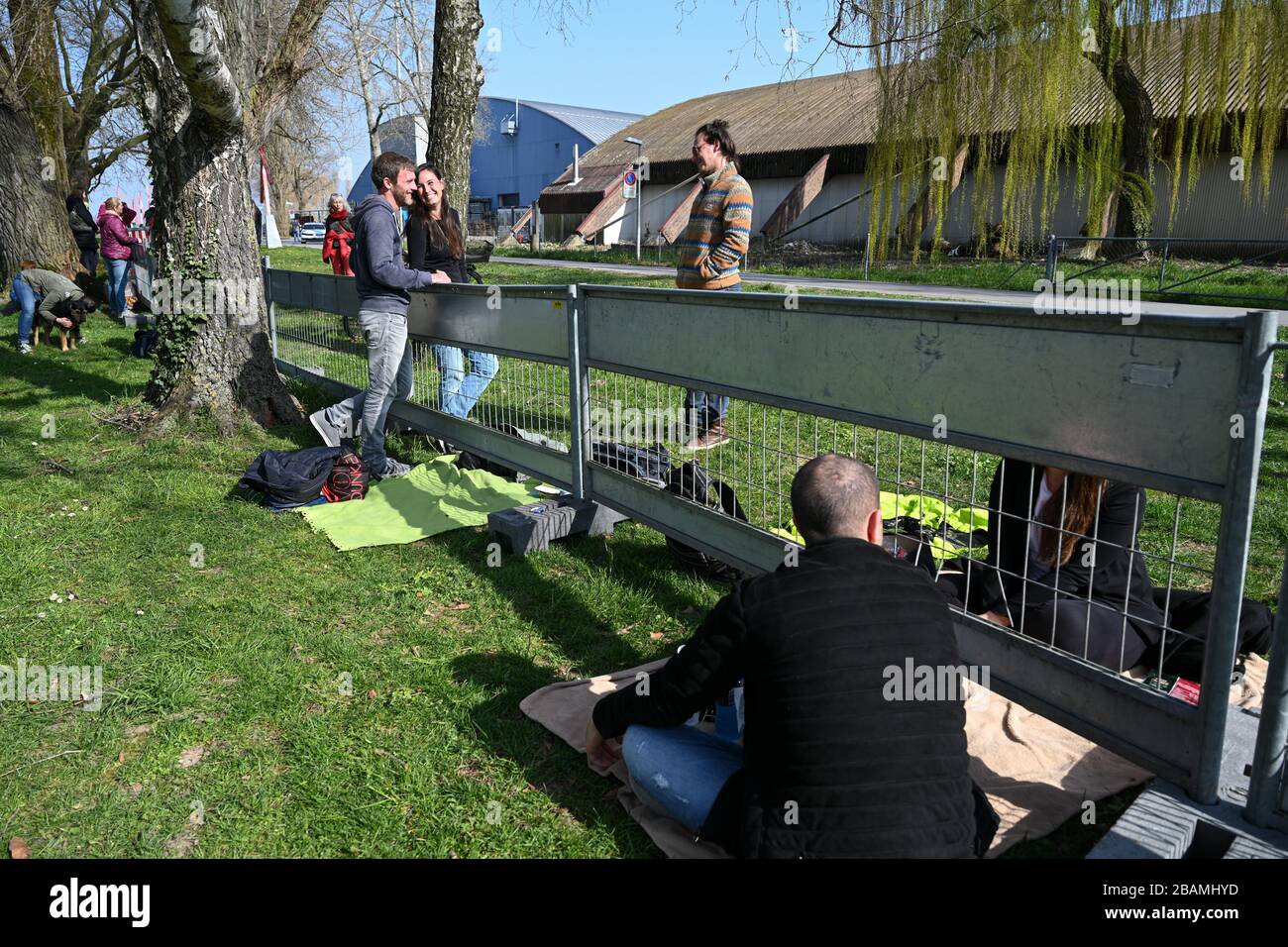 Konstanz, Germania. 26 marzo 2020. Diverse coppie stanno chiacchierando sul confine tedesco-svizzero tra Costanza e Kreuzlingen. Le coppie sono separate da un recinto di confine e questo è l'unico modo per abbracciare e incontrare. Decine di coppie e famiglie si sono incontrate per vedersi al confine lungo diverse centinaia di metri, normalmente aperto a pedoni e ciclisti. La polizia svizzera e un servizio di sicurezza controllano la distanza tra le coppie e le famiglie. Credit: Felix Kästle/dpa/Alamy Live News Foto Stock