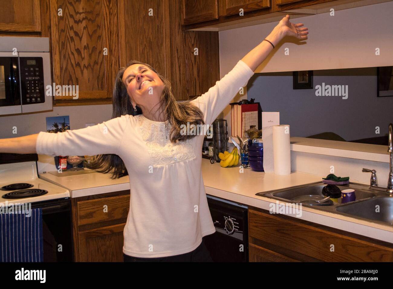 Donna felice nella sua cucina con le braccia spalmato sorridendo Foto Stock