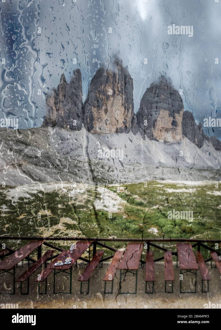 Tre Cime si innalza nelle Dolomiti italiane attraverso una finestra di rifugio coperta di gocce di pioggia. Foto Stock