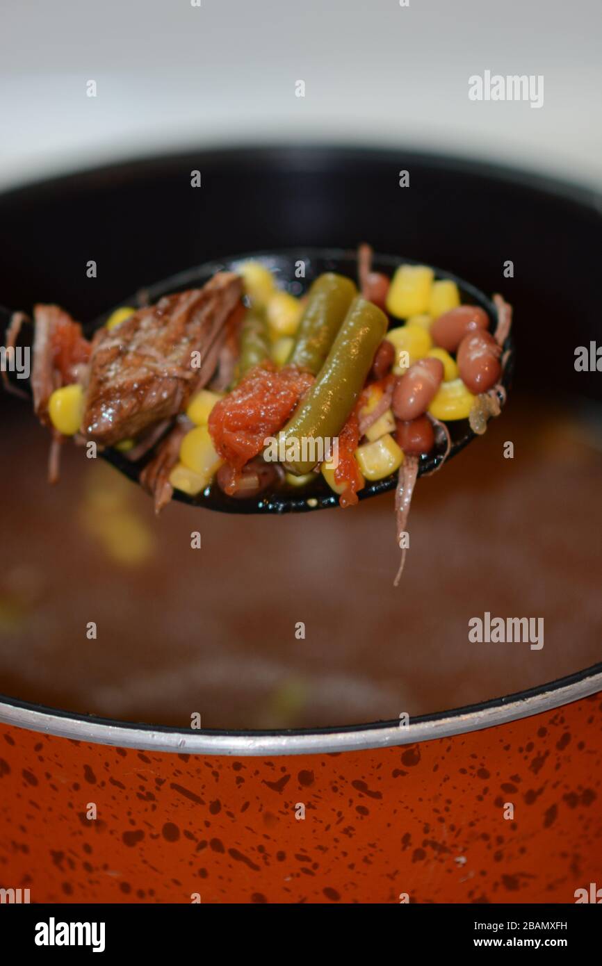 Ampio cucchiaio che offre abbondante zuppa di manzo e verdura fatta in casa da una pentola. Primo piano. Colorato. Foto Stock