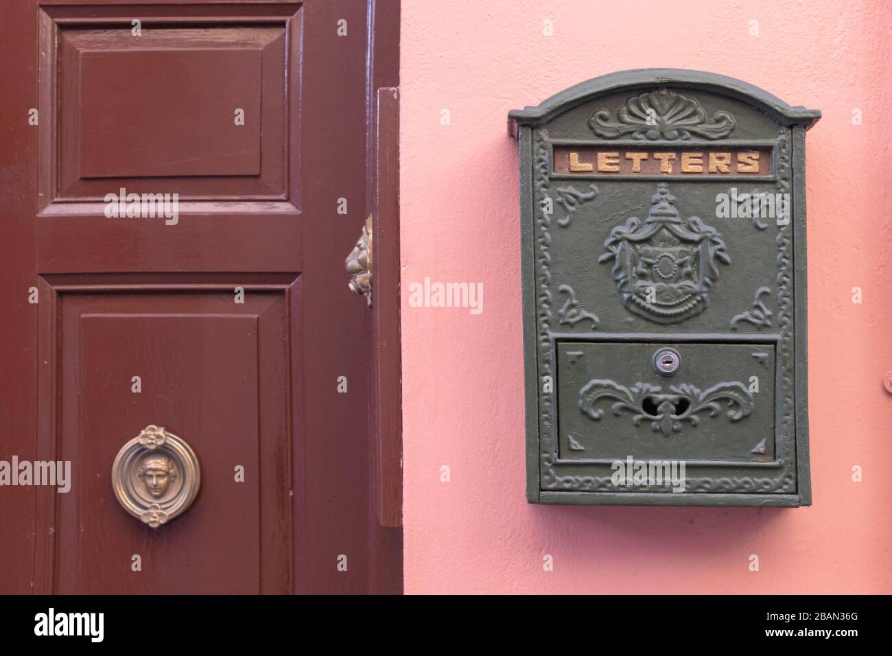 Una casella postale verde dall'aspetto retrò brillante, o scatola di lettere, fissata alla parete esterna di una casa rosa. C'è una porta marrone con pomello dorato Foto Stock