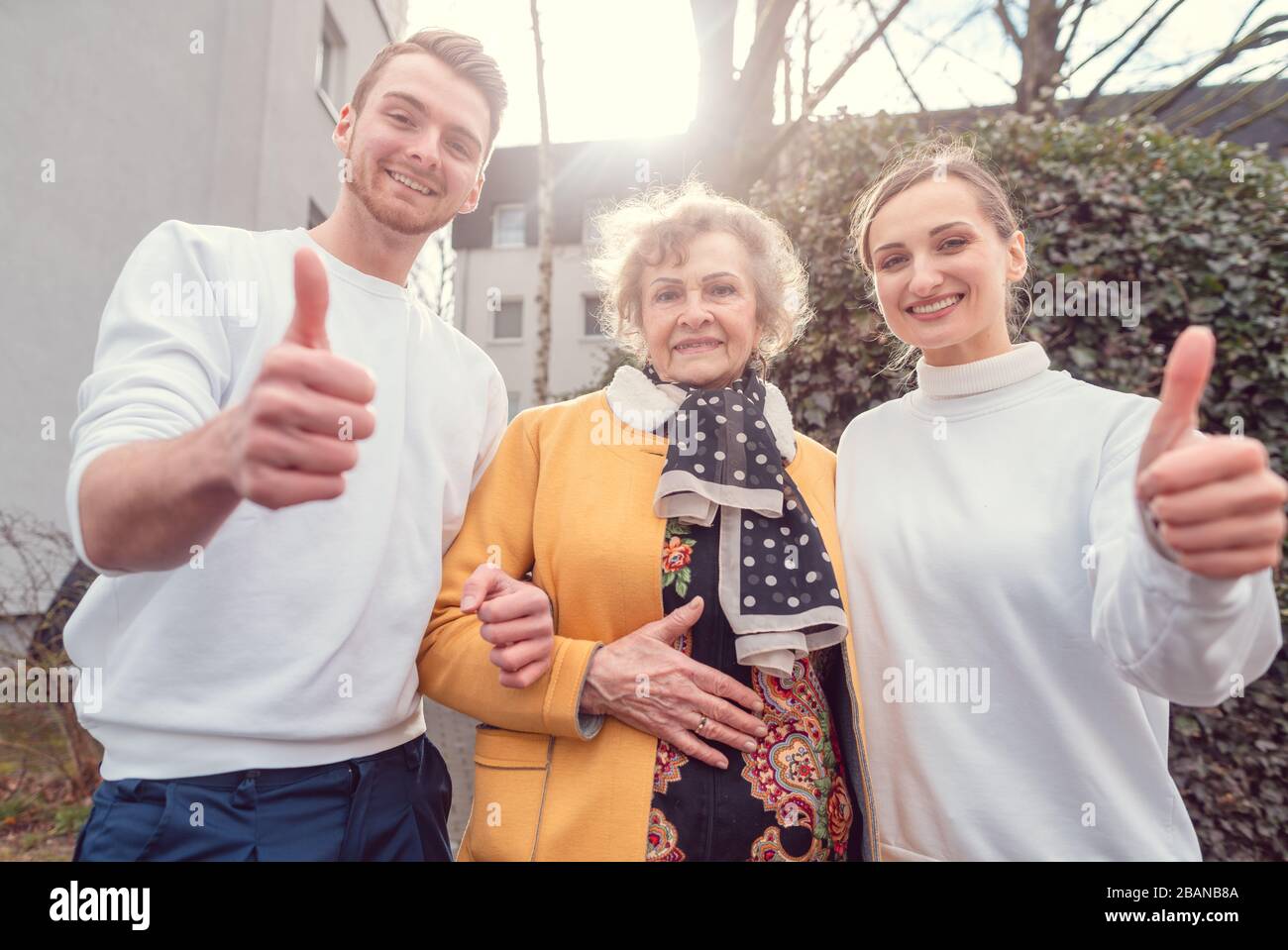 Due aiutanti del servizio sociale e signora anziana che dà i pollici in su Foto Stock