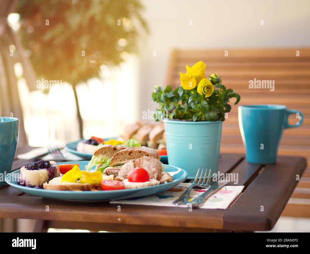 Bella e colorata cornice per la colazione primaverile con una varietà di cibo su un tavolo di legno con fiori in una giornata di sole. Foto Stock