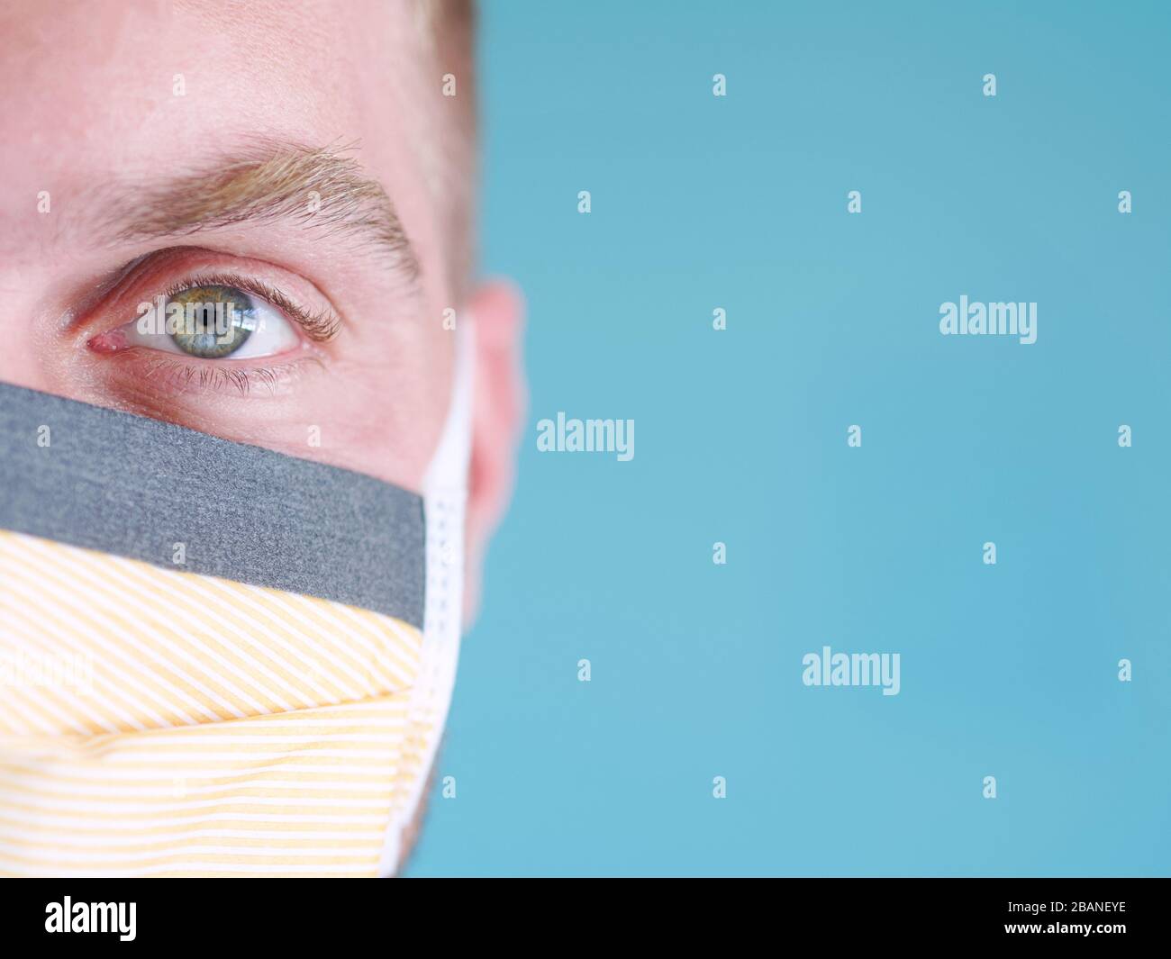 Closeup di un uomo caucasico viso indossare maschera di protezione viso giallo con occhi verdi e capelli biondi, dal nuovo focolaio di coronavirus. Foto Stock