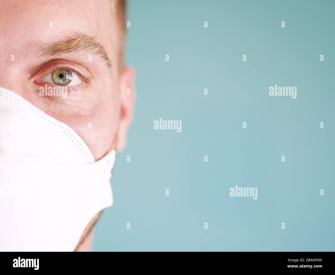 Closeup di un uomo caucasico viso indossare maschera di protezione viso giallo con occhi verdi e capelli biondi, dal nuovo focolaio di coronavirus. Foto Stock