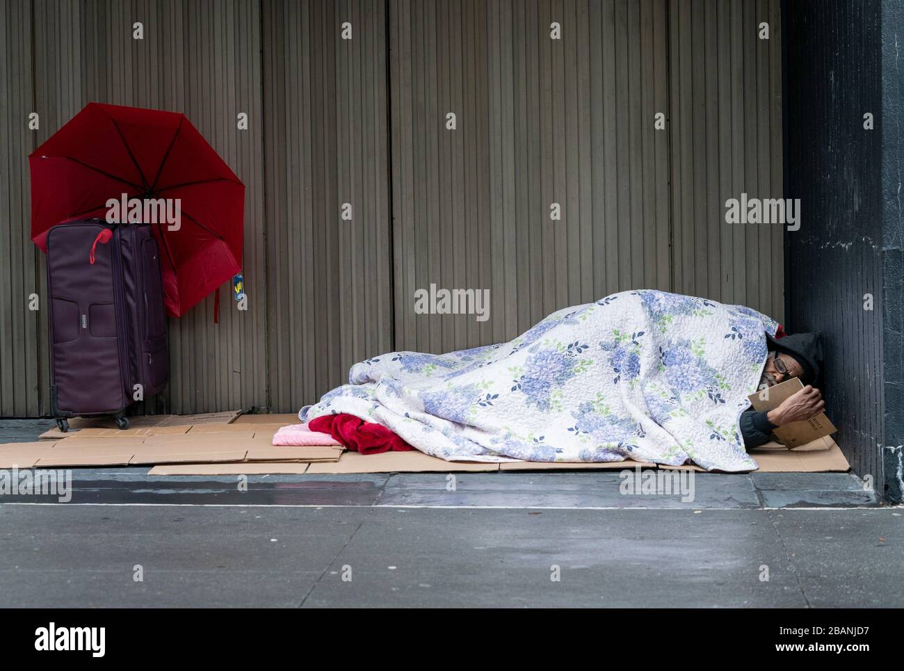 New York, NY - 28 marzo 2020: I senzatetto giace sotto coperta sulla strada e legge la Sacra Bibbia a Manhattan Foto Stock