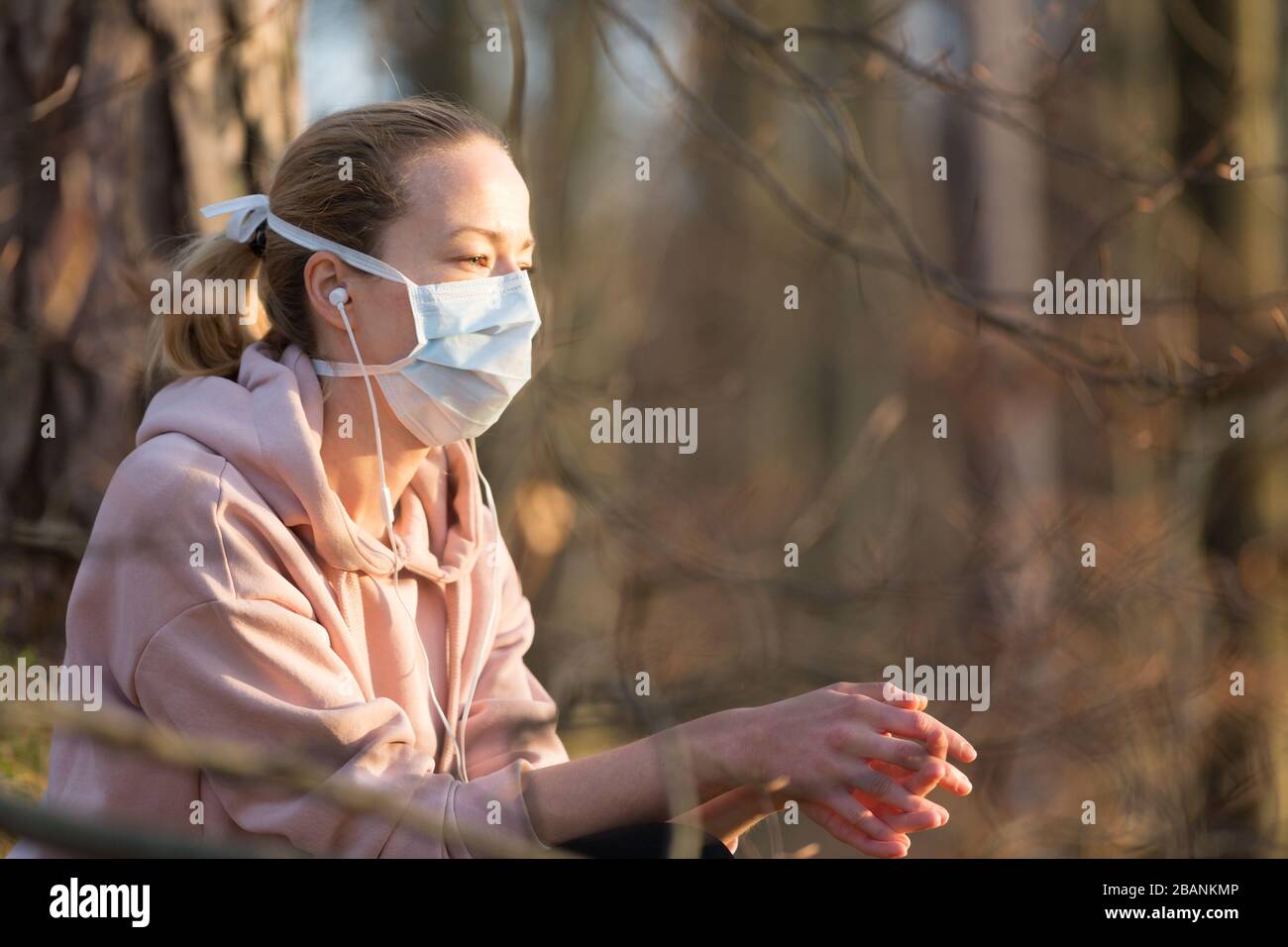 Ritratto della donna sportiva caucasica che indossa la maschera facciale di protezione medica mentre si rilassa nella natura e si ascolta la musica. Il virus Corona, o Covid-19, è Foto Stock
