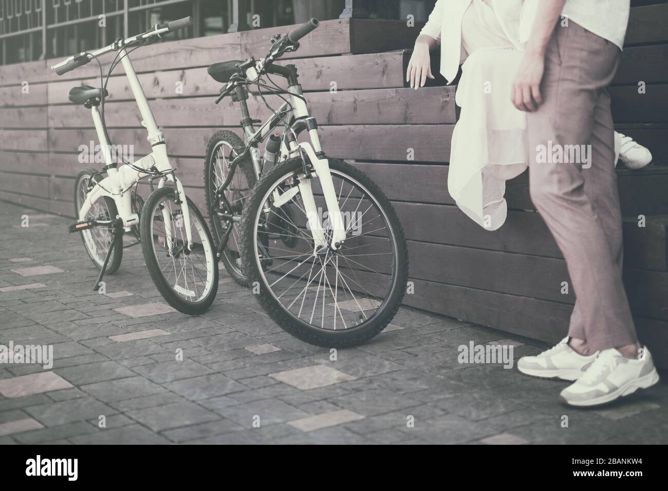 Vista sulle gambe dell'uomo accanto a due biciclette su un marciapiede Foto Stock