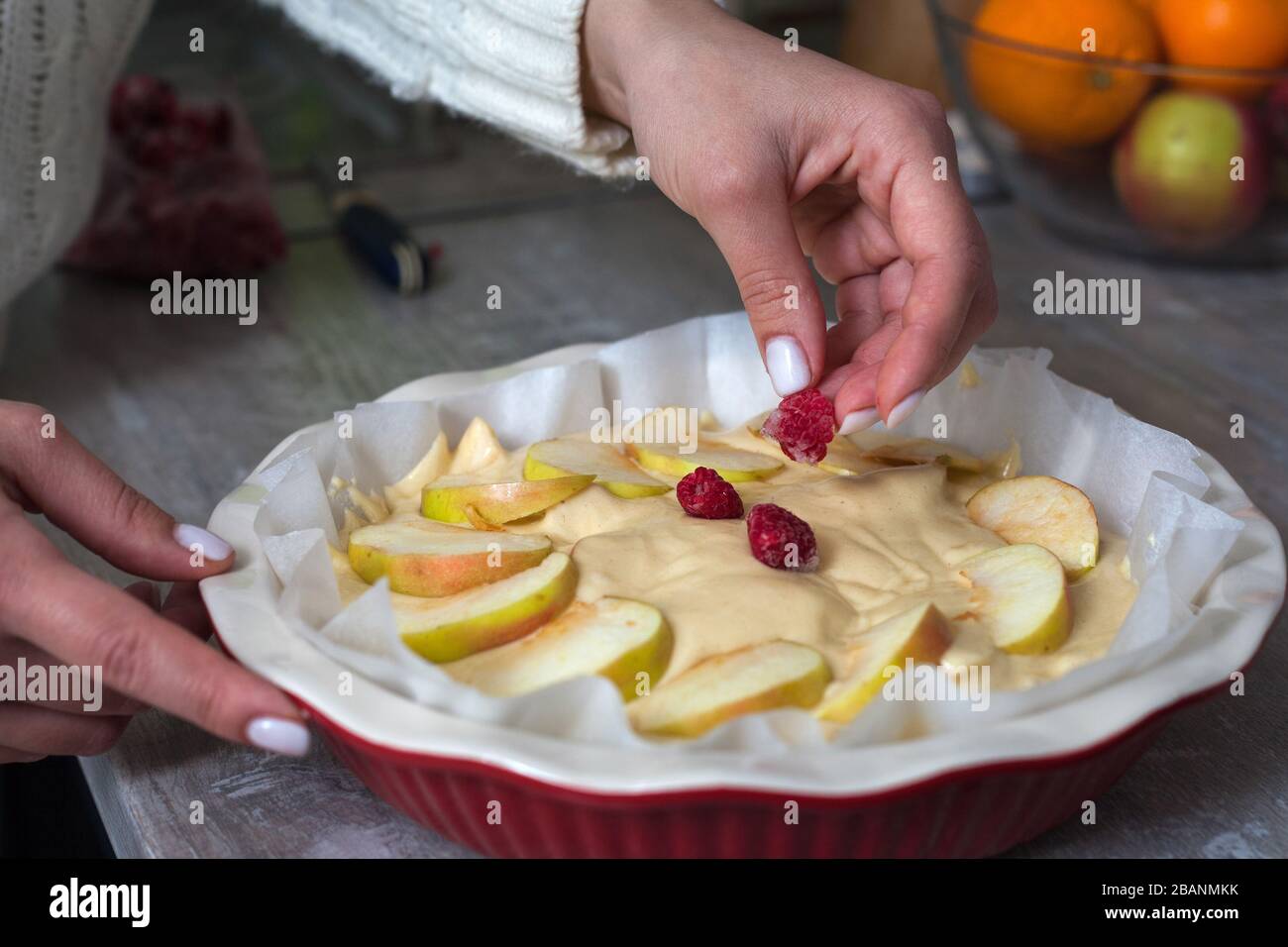 La padrona di casa sta preparando la mela charlotte in cucina. Mette il bacche su una torta di mele in un piatto da forno. Pasta di mele cruda Foto Stock