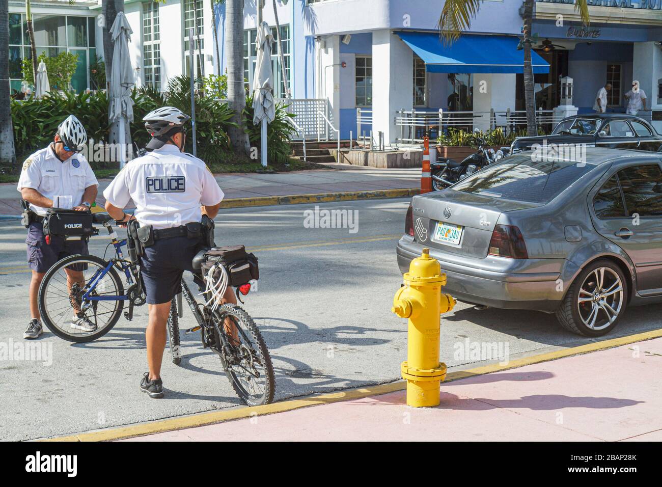 Miami Beach Florida, Ocean Drive, polizia, poliziotto, poliziotti, pattuglia bicicletta, dando, emissione, biglietto, auto parcheggiate illegalmente, veicolo, da idrante incendio, visi Foto Stock