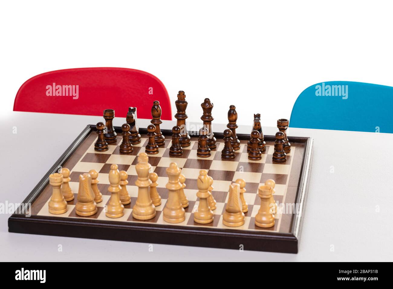 Chessboard su un tavolo pronto per il gioco con sedie per bambini sullo sfondo. Foto Stock