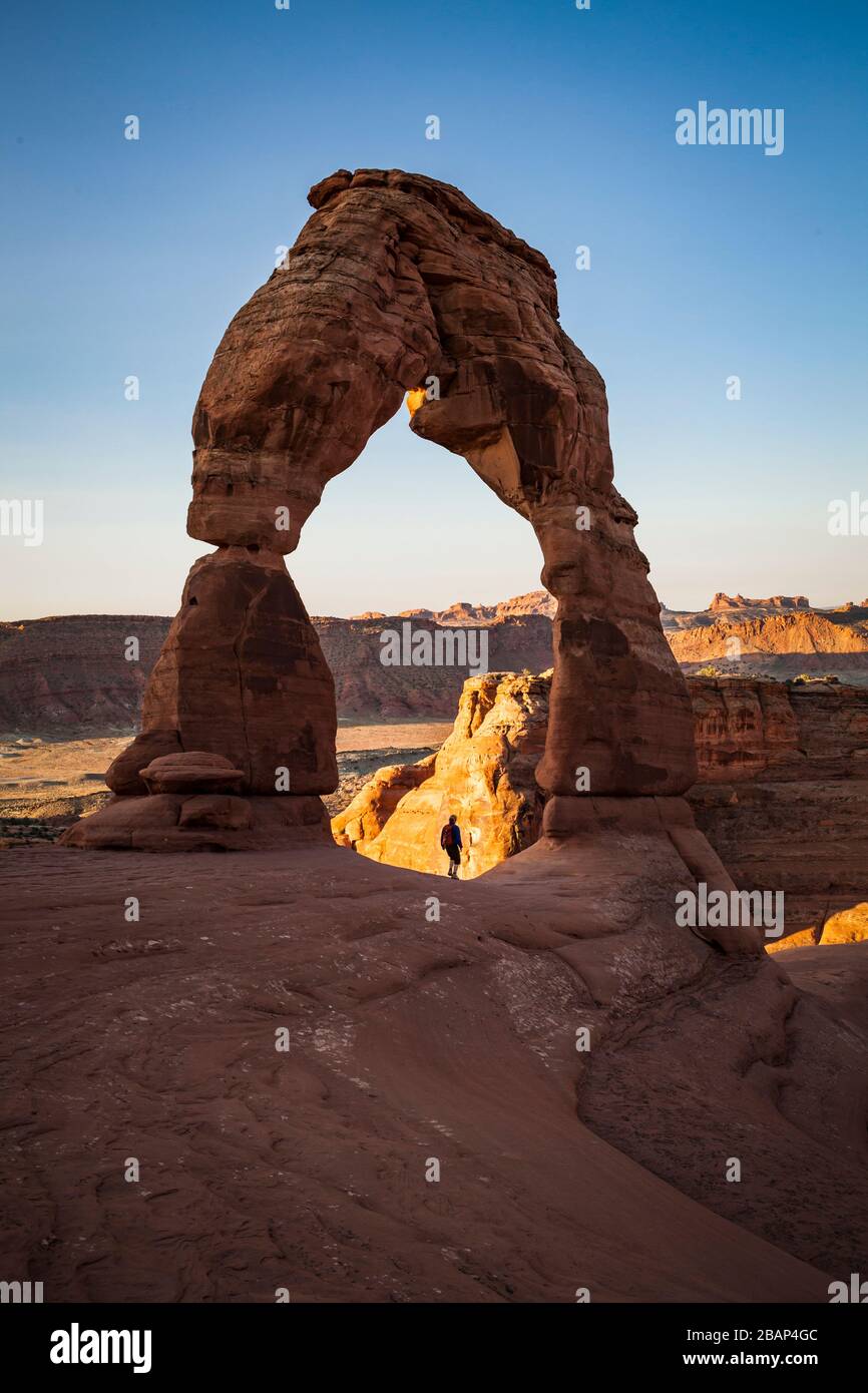 Un'escursionista solista passa sotto il delicato Arch National Park all'alba, Utah, USA. Foto Stock