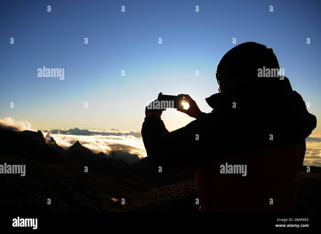 Alpinista scattando una foto al cellulare dell'alba a Pedra do Açú (2.245 m) nel Parco Nazionale Serra dos Órgãos, al punto più alto della città di Foto Stock