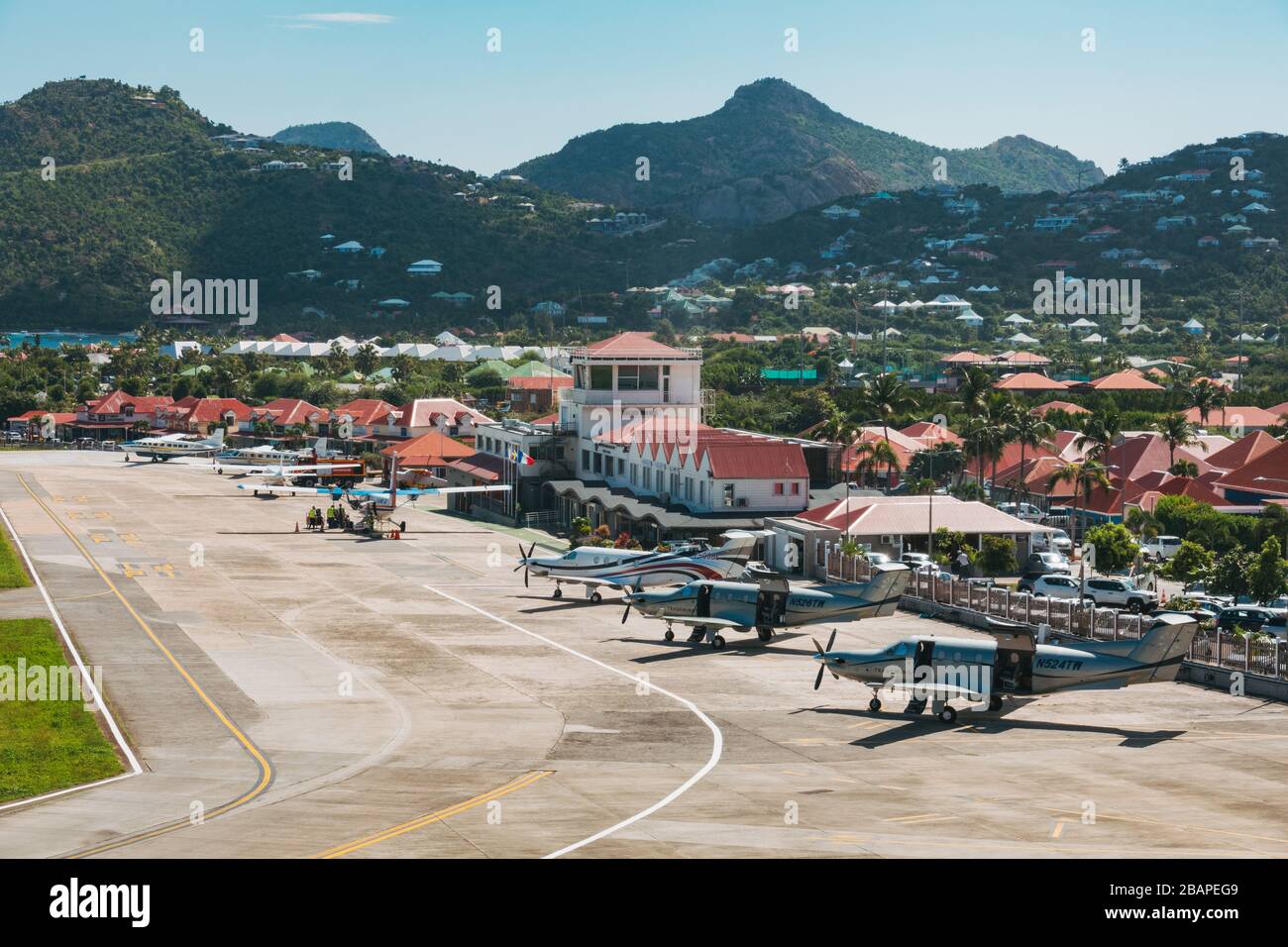 Una fila di aerei parcheggiati di fronte al piccolo edificio del terminal dell'aeroporto di Saint Barthélemy Foto Stock