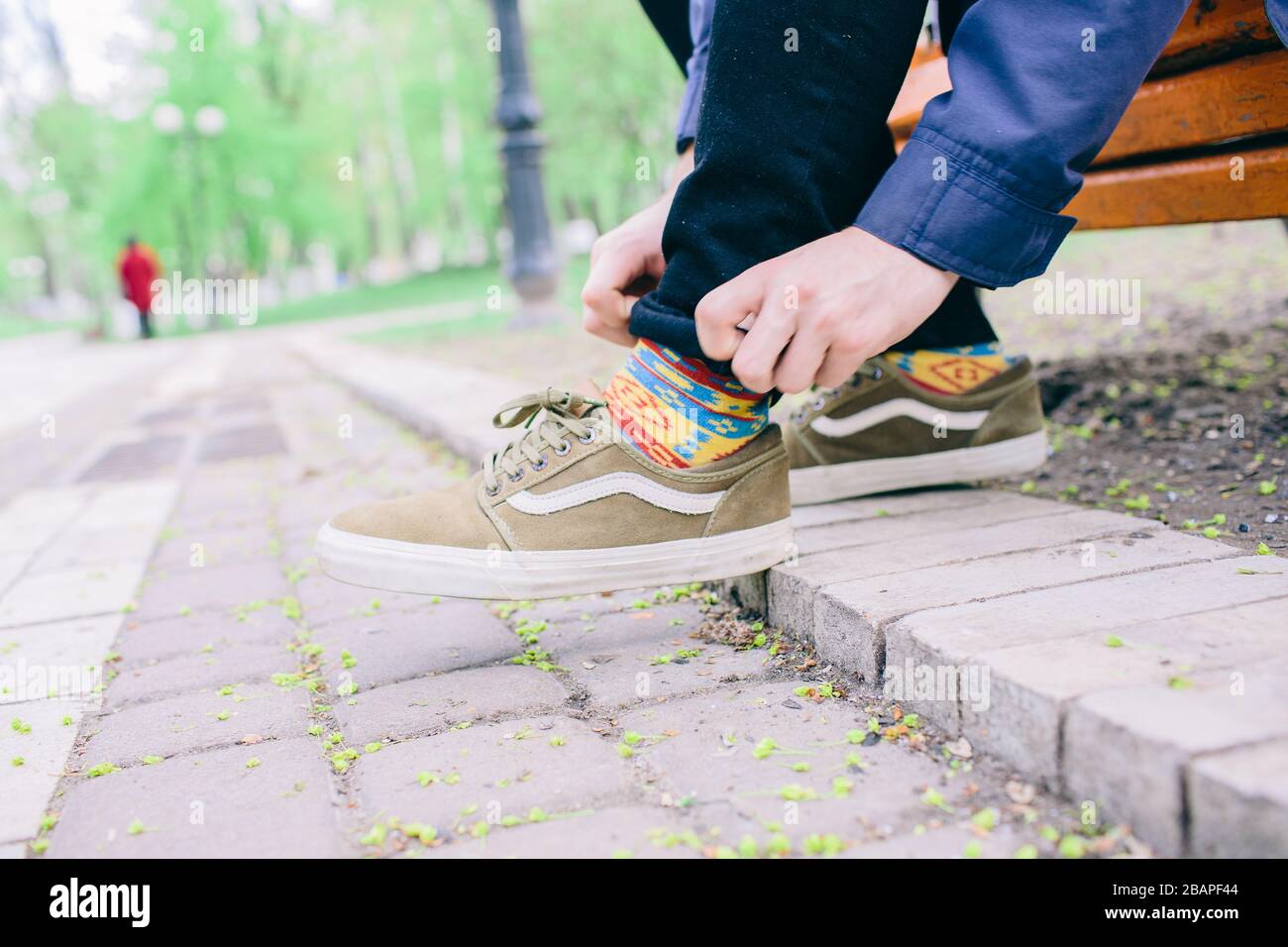 Uomo in pende e scarpe da ginnastica siedono su panche e lacci scarpe  cravatte. Solo in parco e all'aperto. Arrotolare il bordo dei pantaloni.  Preparati Foto stock - Alamy