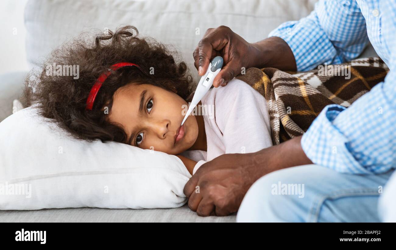 Concetto di malattia infettiva. Figlio americano malato e suo nonno con termometro a casa Foto Stock