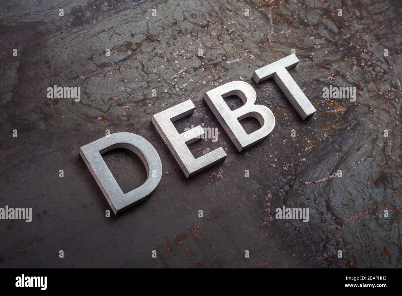 la parola debito disposto con lettere argento su grezzo arrugginito lamiera di acciaio in prospettiva diagonale inclinata con fuoco selettivo e sfocatura sfondo Foto Stock