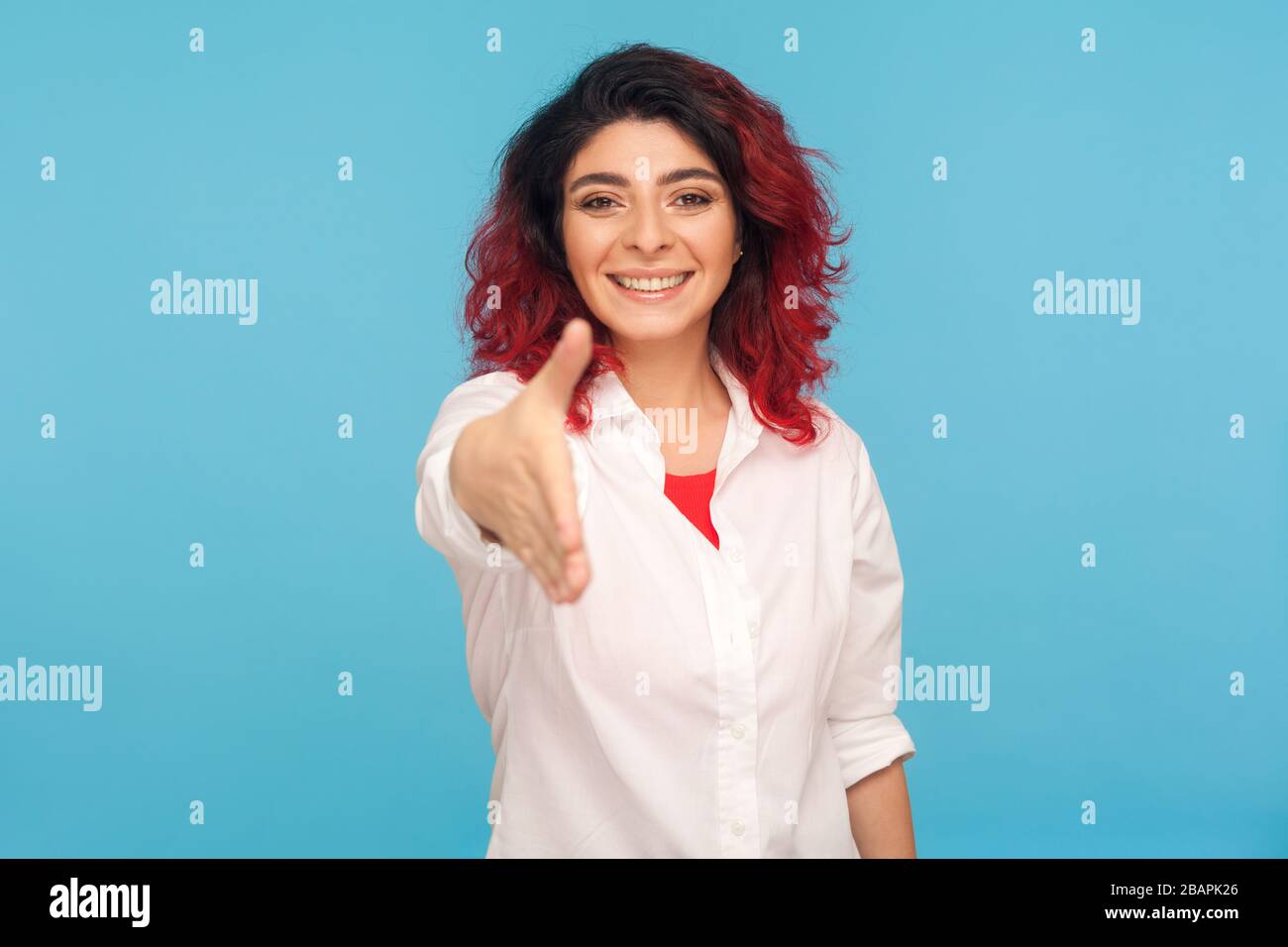 Piacere di incontrare, benvenuto! Ritratto di socievole donna hippster con fantasia capelli rossi in camicia dando mano a stretta di mano e sorridente amichevole, dicendo congrats. Foto Stock