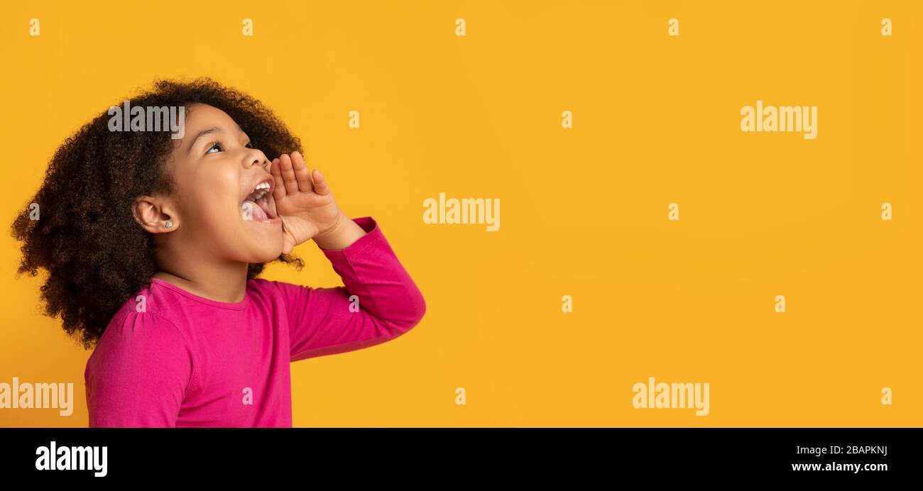 Cute ragazza afroamericana piccola gridando a copia spazio, facendo l'annuncio Foto Stock