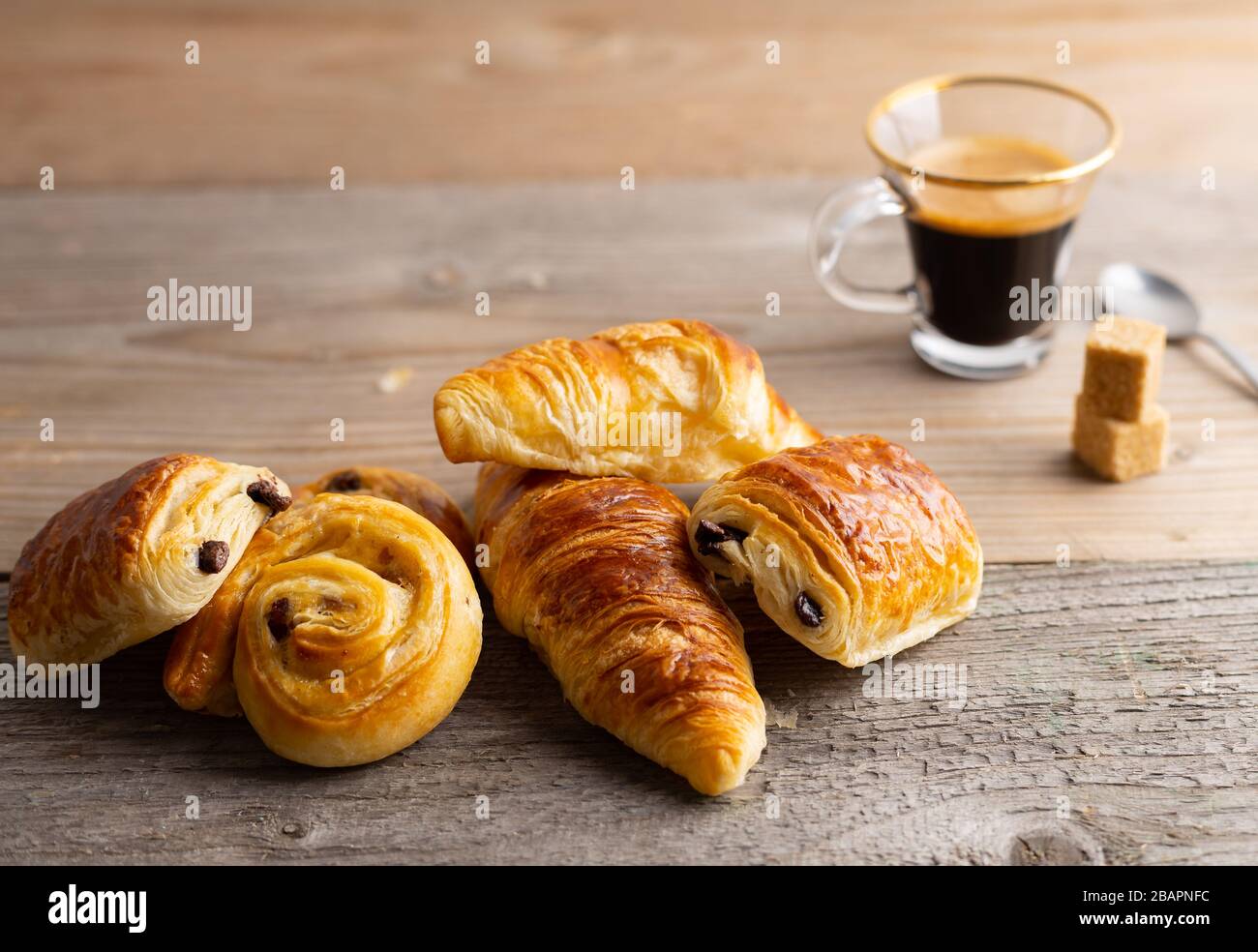 Colazione con croissant, dolci alla cannella e cioccolato, succo d'arancia fresco e caffè sul lato su sfondo di legno. Foto Stock