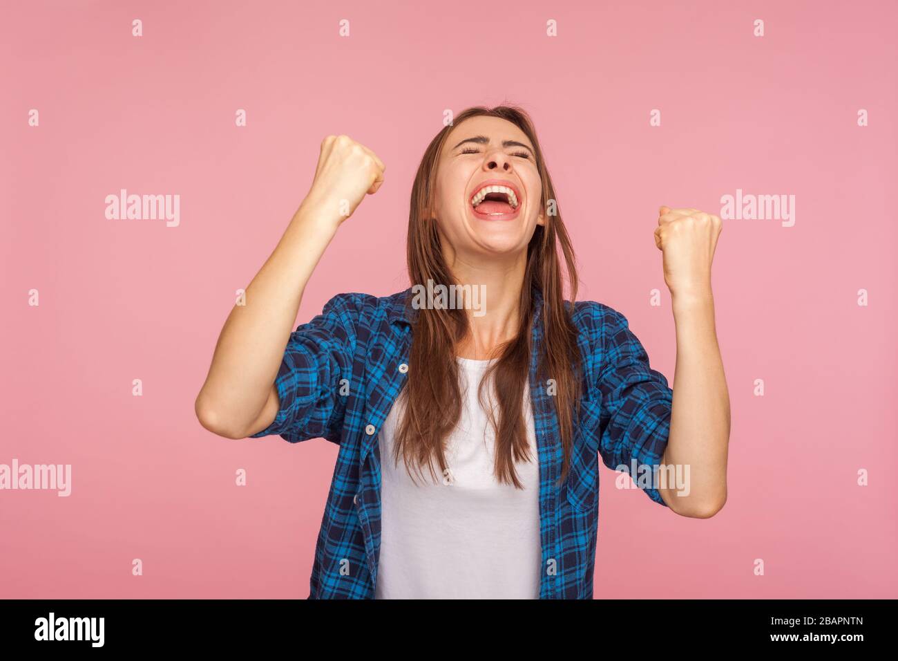 Sono campione! Ritratto di estatica ragazza di successo in camicia a scacchi urlando di gioia con i pugni alzati, celebrando la vittoria, incredibile vittoria. io Foto Stock