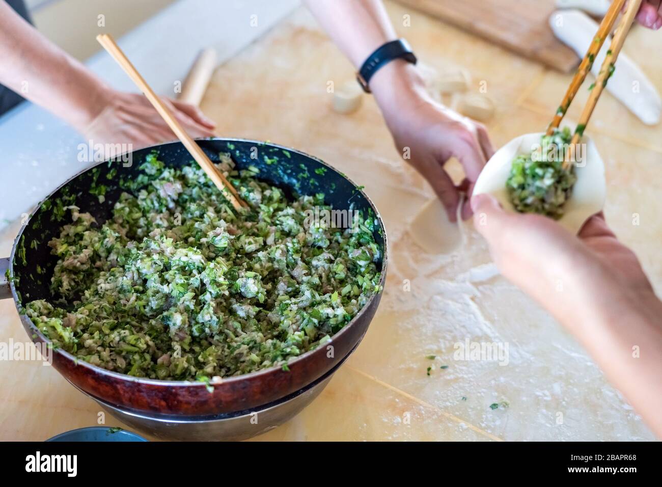 Famiglia cinese che fa gnocchi insieme. Mani che filano ravioli fatti in casa in cucina. Foto Stock
