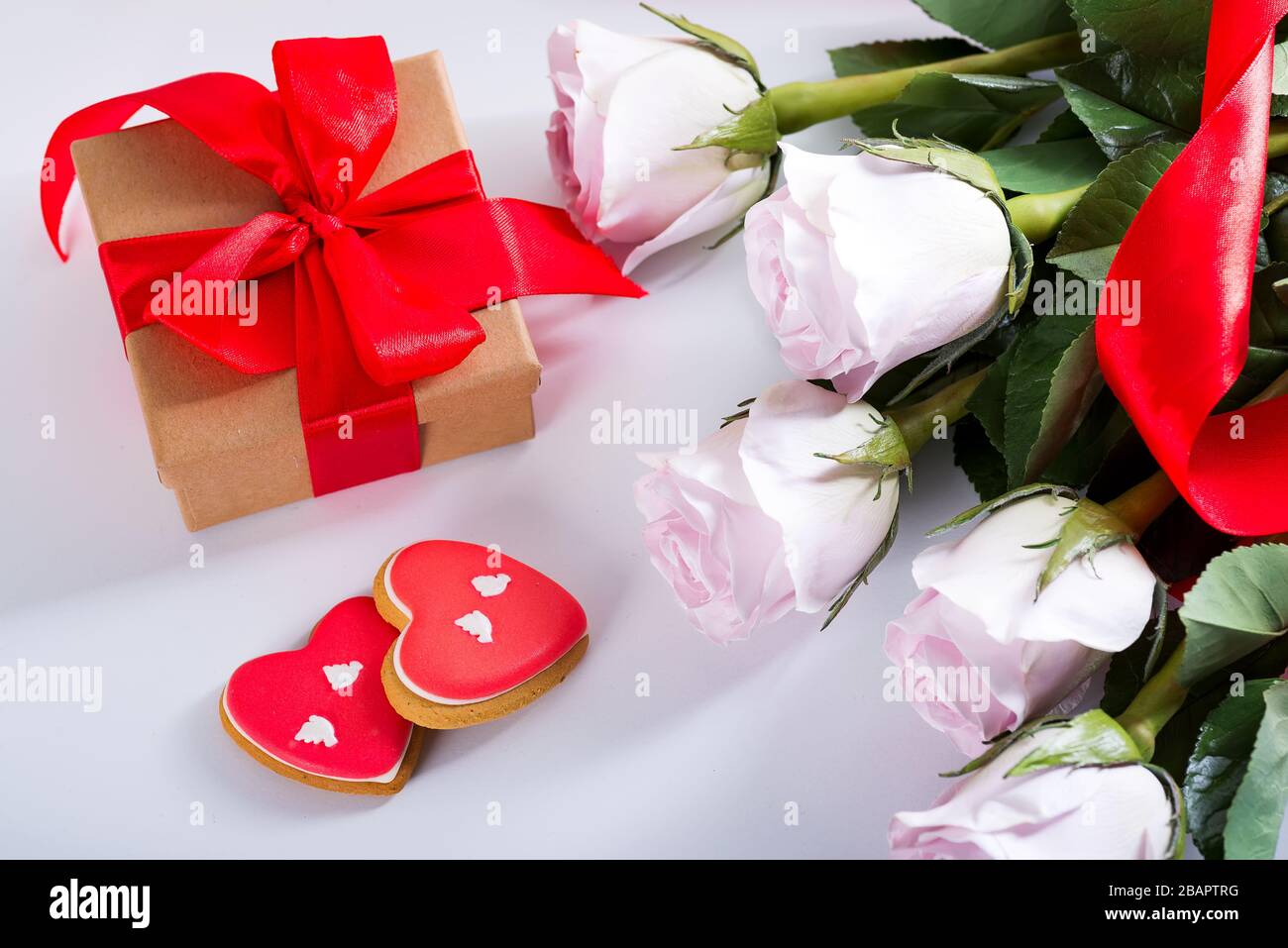 Biscotti fatti in casa di San Valentino cuore, rose rosa e scatola regalo rosso sul tavolo bianco Foto Stock