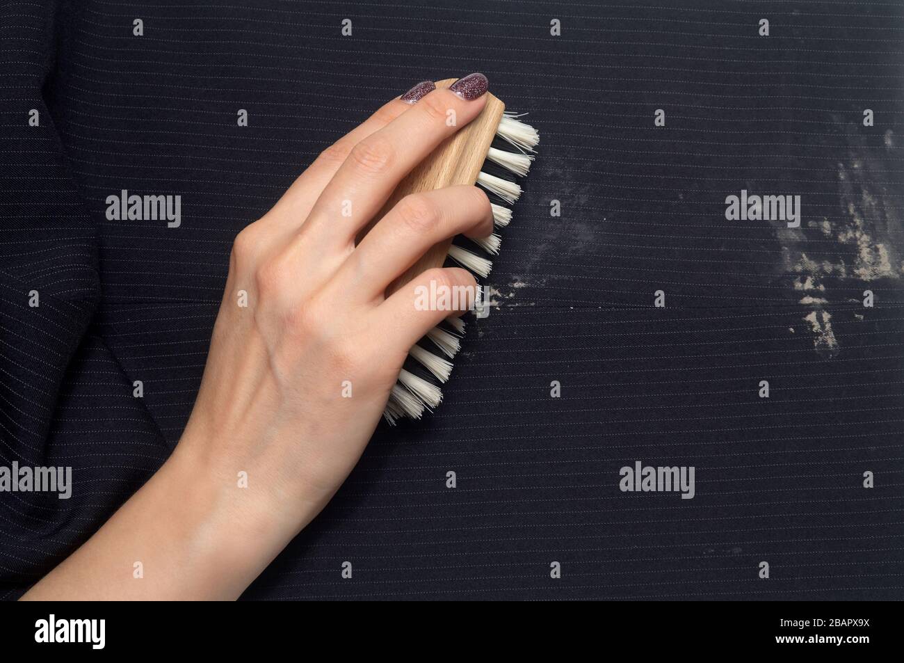 Lavaggio a secco: Una mano da donna con un pennello per la pulizia dei vestiti da sporco Foto Stock