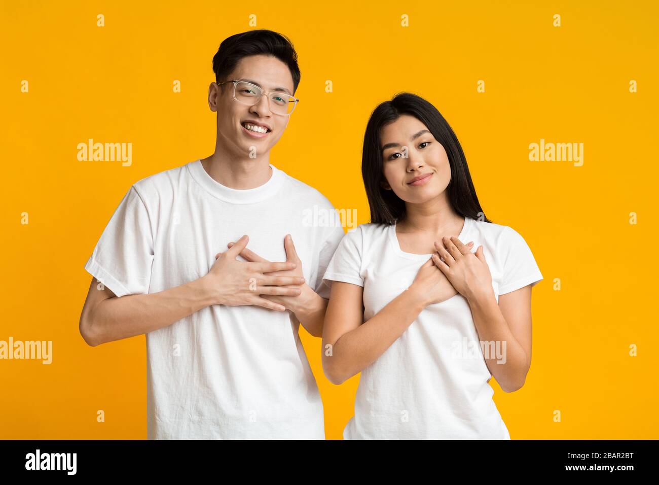 Gentile donna asiatica e uomo tenere entrambe le palme sul petto Foto Stock