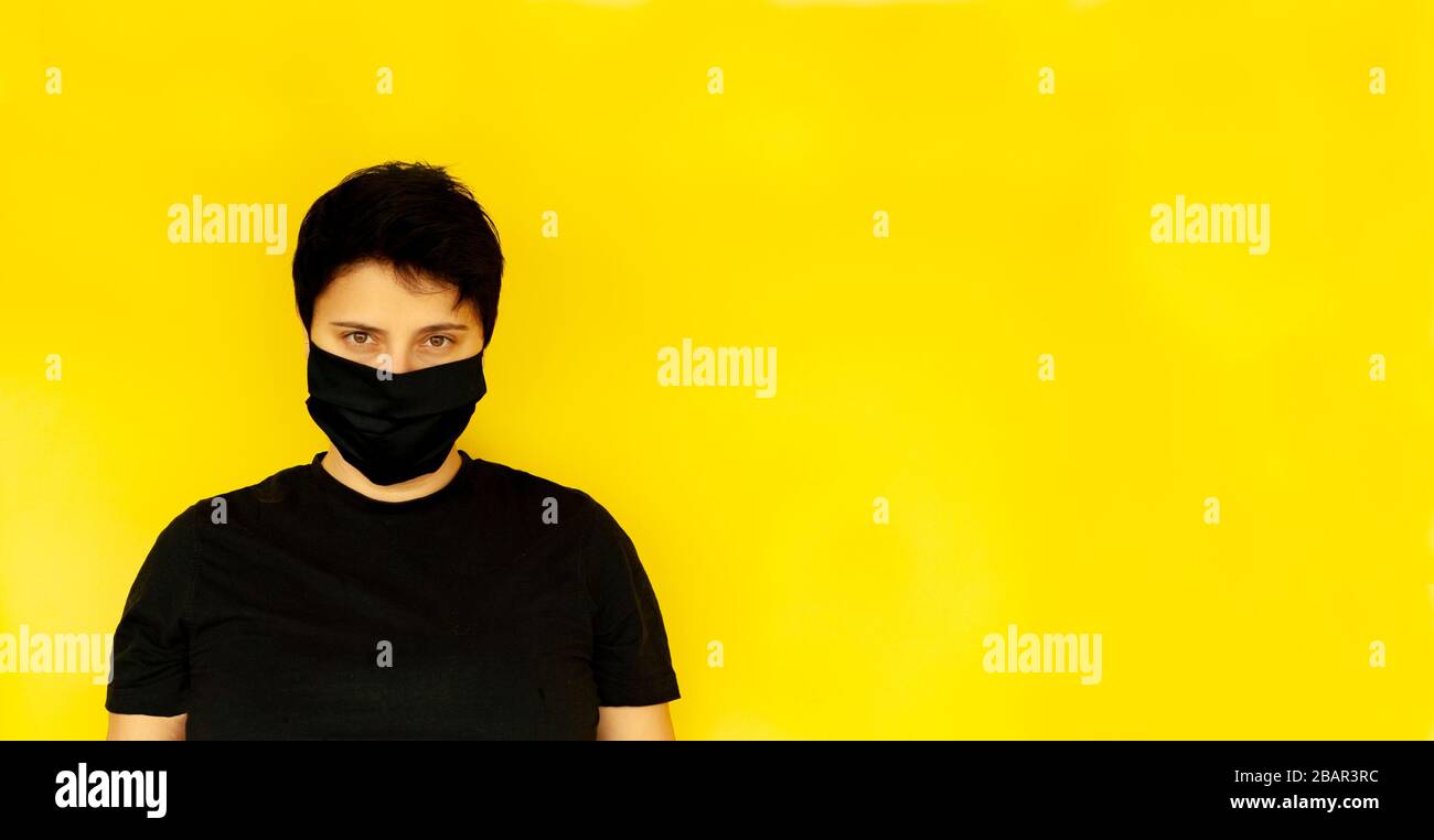 Ragazza brunette capelli corti LGBT maschera nera grave aspetto giallo sfondo, banner. Coronavirus Foto Stock