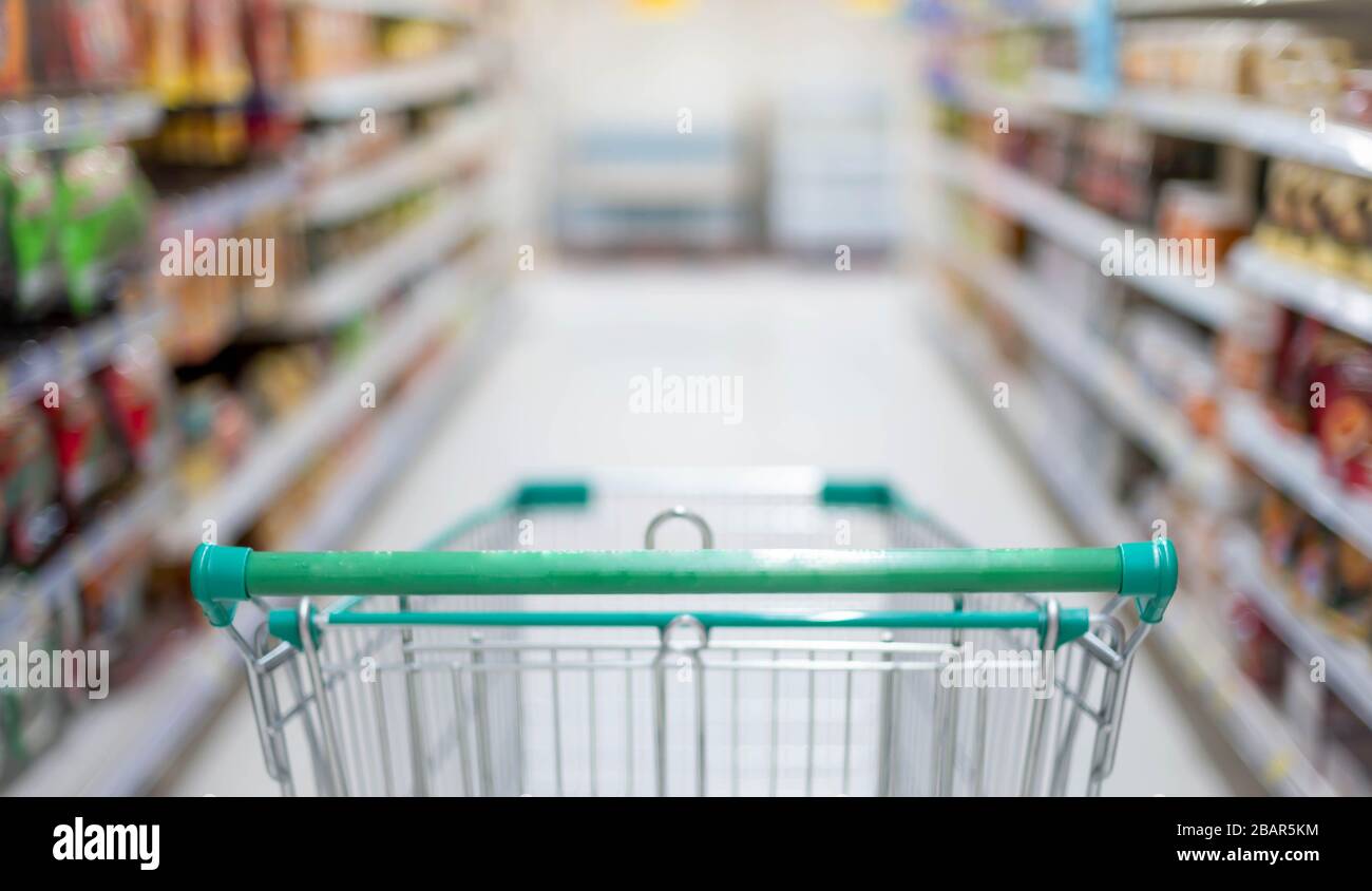 Effetto sfocato nella corsia Supermarket con carrello vuoto per lo shopping in argento e verde, Shopper scegliere il cibo in supermercato Panic acquirente per hoardi Foto Stock