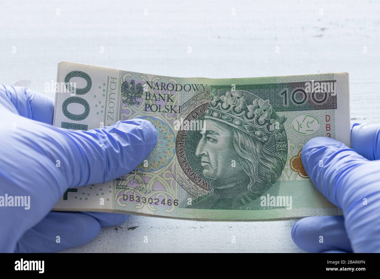 Denaro polacco, cento zlotys banconote tenute in guanti di gomma. Il concetto di economia e minacce finanziarie durante la pandemia di Coronavirus Foto Stock