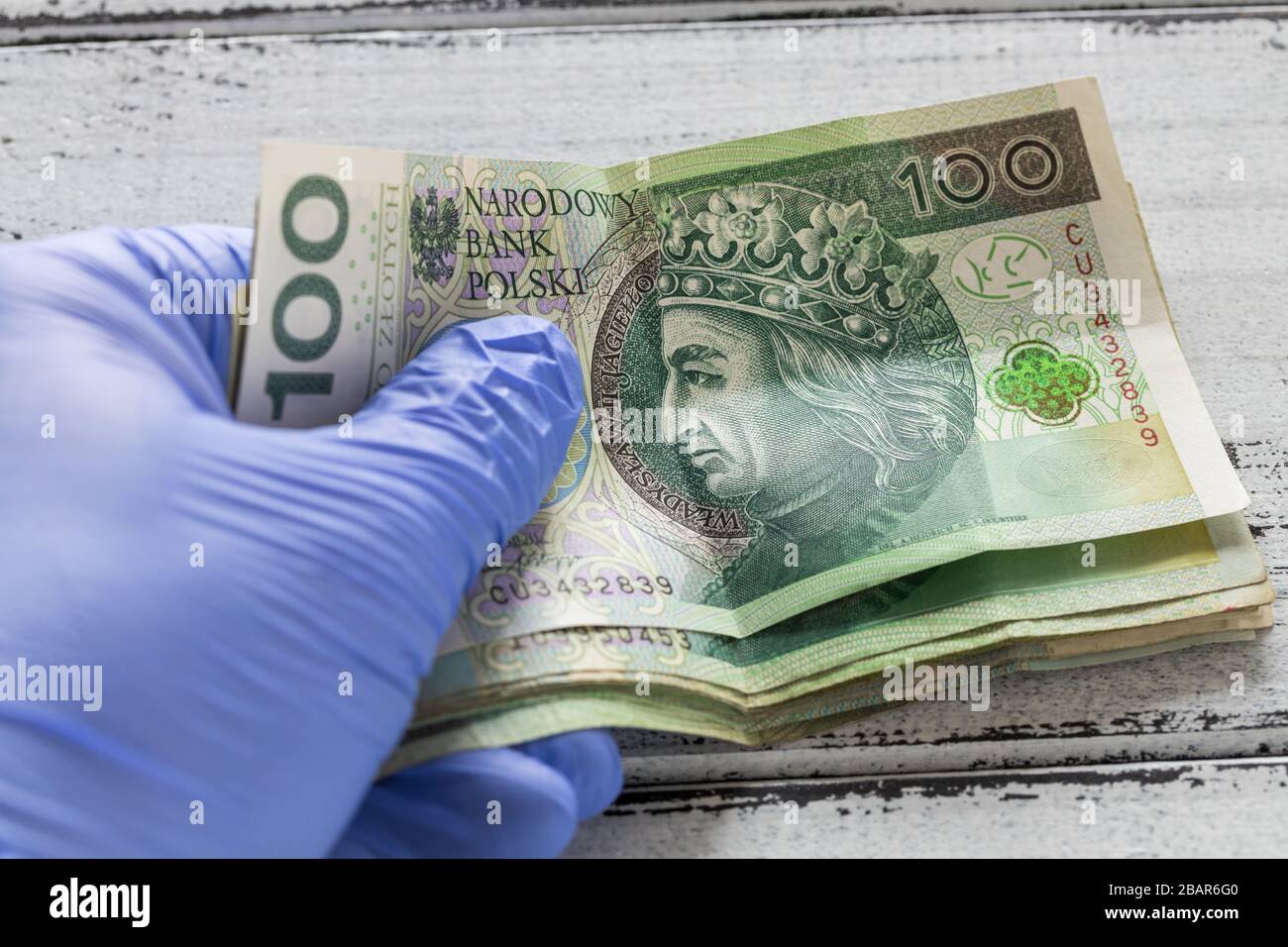 Denaro polacco, cento zlotys banconote tenute in guanti di gomma. Il concetto di economia e minacce finanziarie durante la pandemia di Coronavirus Foto Stock