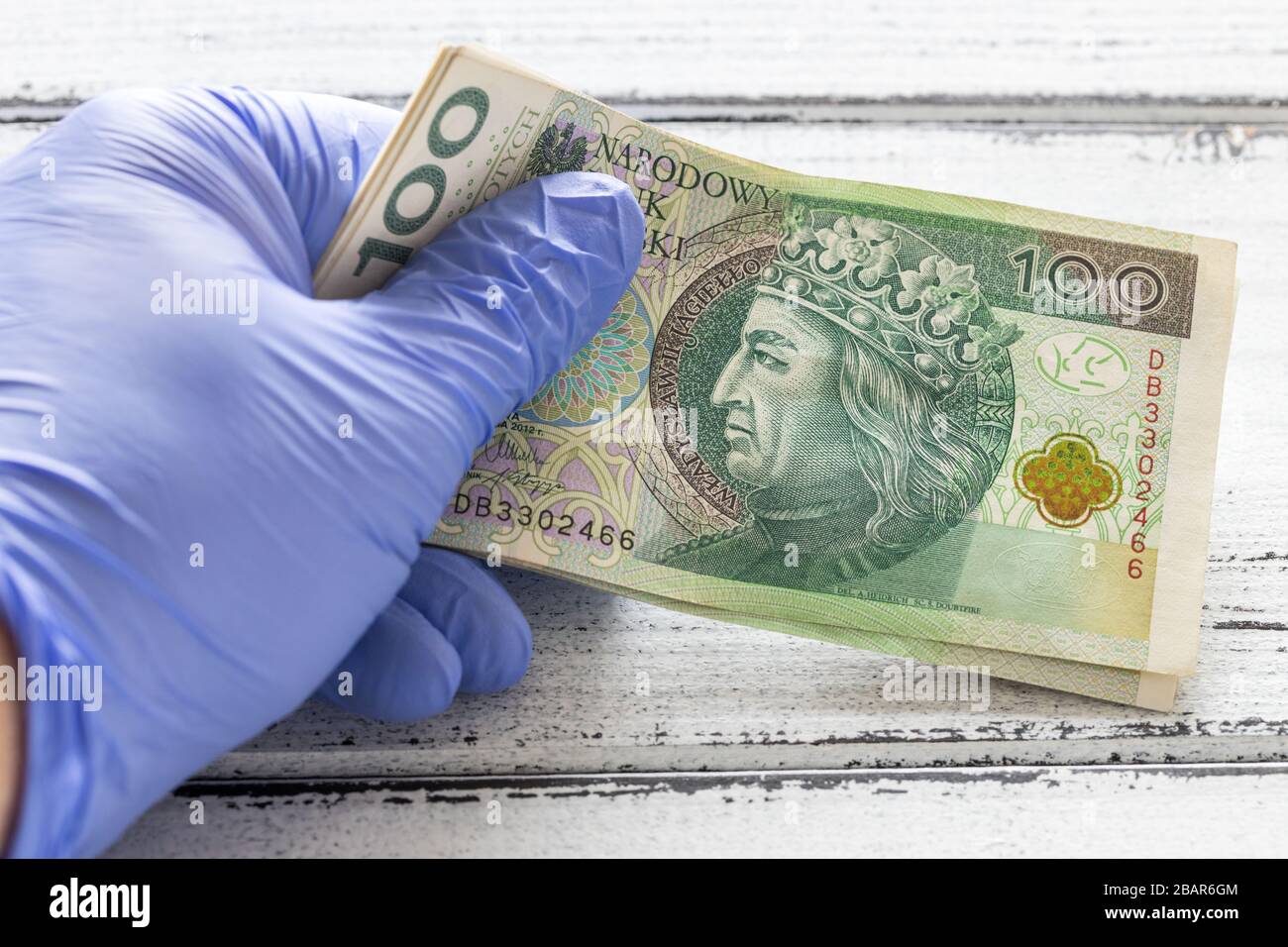 Denaro polacco, cento zlotys banconote tenute in guanti di gomma. Il concetto di economia e minacce finanziarie durante la pandemia di Coronavirus Foto Stock