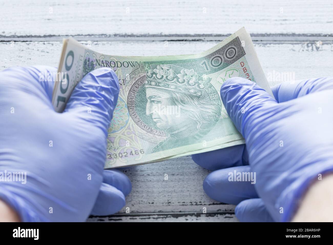 Denaro polacco, cento zlotys banconote tenute in guanti di gomma. Il concetto di economia e minacce finanziarie durante la pandemia di Coronavirus Foto Stock