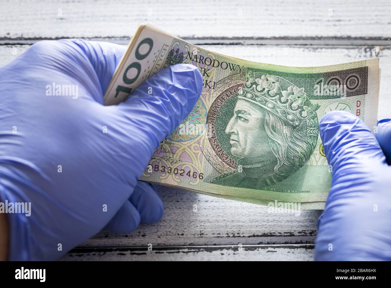 Denaro polacco, cento zlotys banconote tenute in guanti di gomma. Il concetto di economia e minacce finanziarie durante la pandemia di Coronavirus Foto Stock