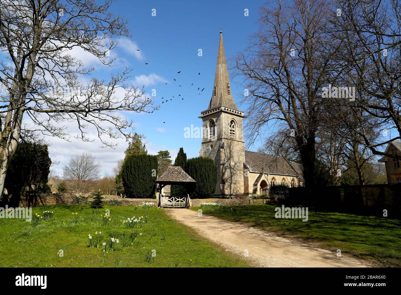 Narcisi che crescono al di fuori della chiesa parrocchiale di Santa Maria nel villaggio di Lower Slaughter nel Cotswolds, Gloucestershire come gli orologi si muovono in avanti di un'ora al British Summer Time (BST). Foto Stock