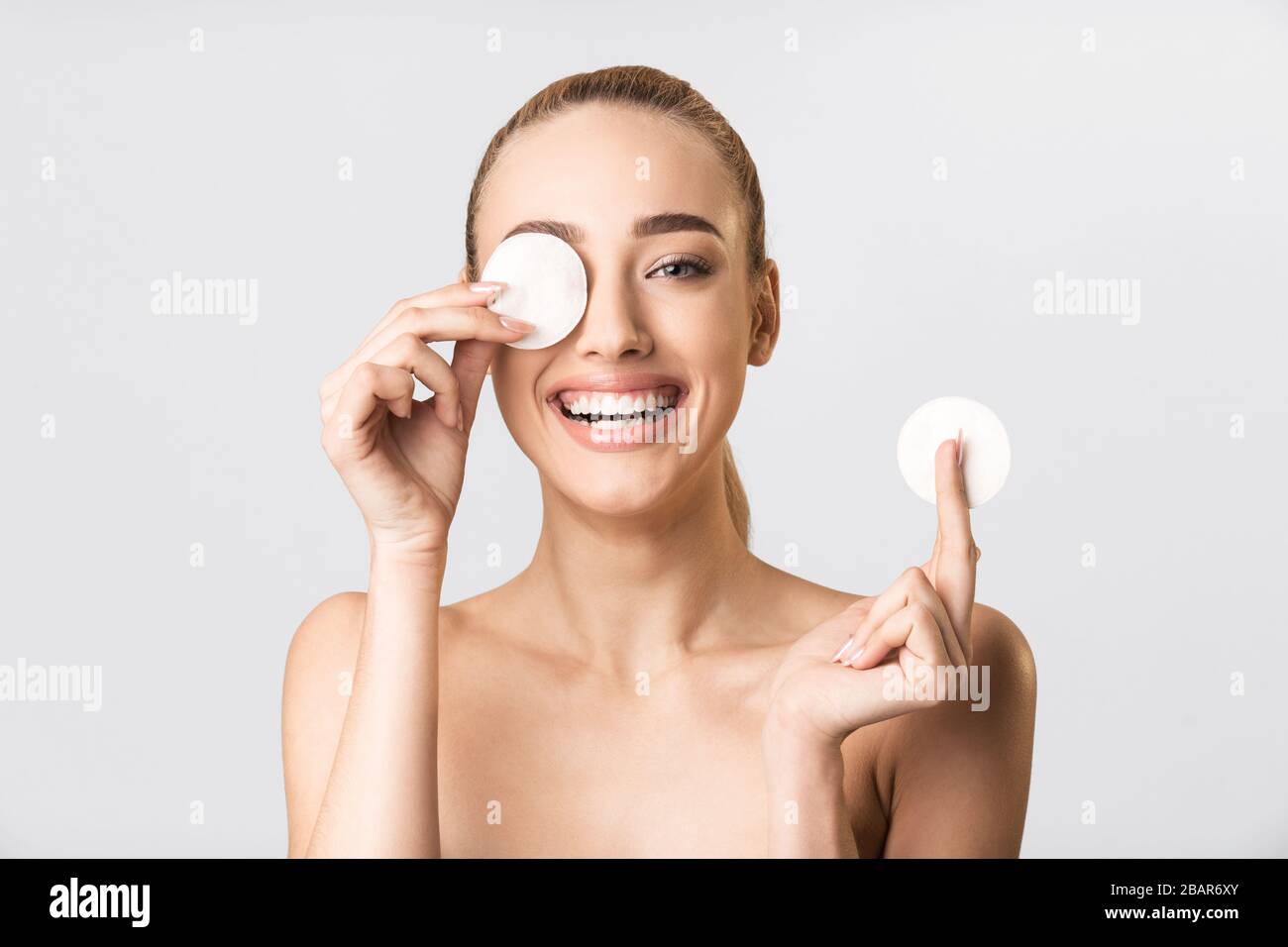 Ragazza bionda che copre l'occhio con il tampone di cotone che ha divertimento, studio Foto Stock