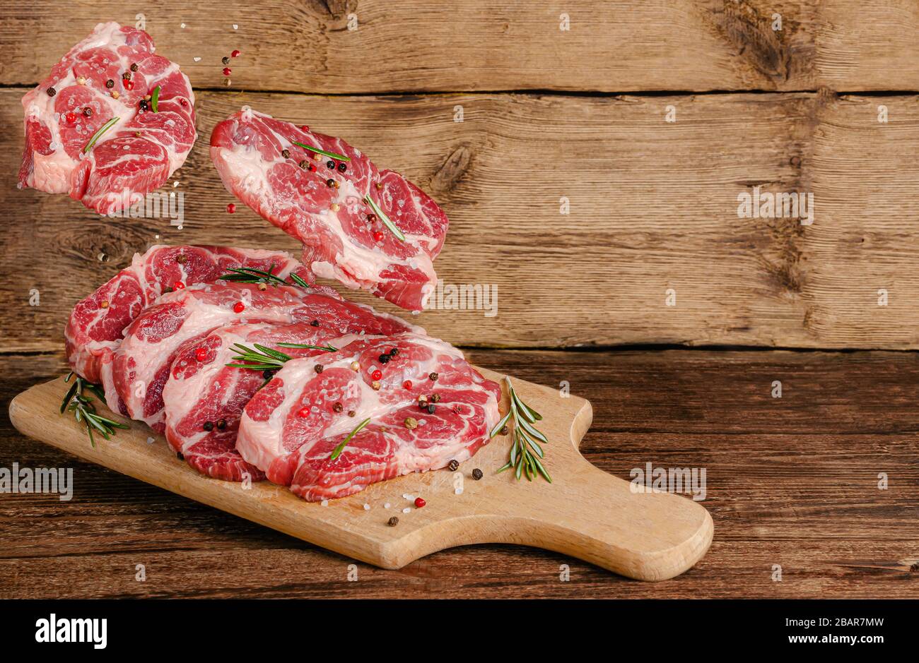 Bistecche di maiale al volo a bordo con carne e spezie su sfondo di legno. Spazio di copia Foto Stock