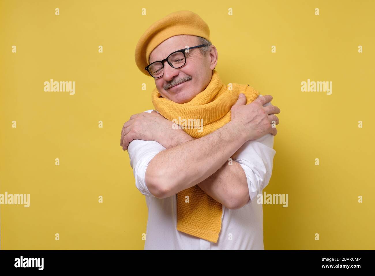 l'uomo in occhiali e cappello giallo e sciarpa si abbraccia, ha un'alta stima di sé Foto Stock