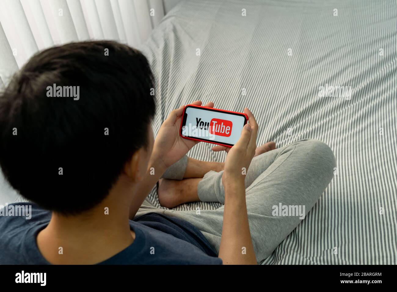 BANGKOK, THAILANDIA - 27 MARZO 2020: Un uomo che tiene un telefono con screenshot di YouTube su iPhone. YouTube è il popolare sito Web per la condivisione di video online. Foto Stock