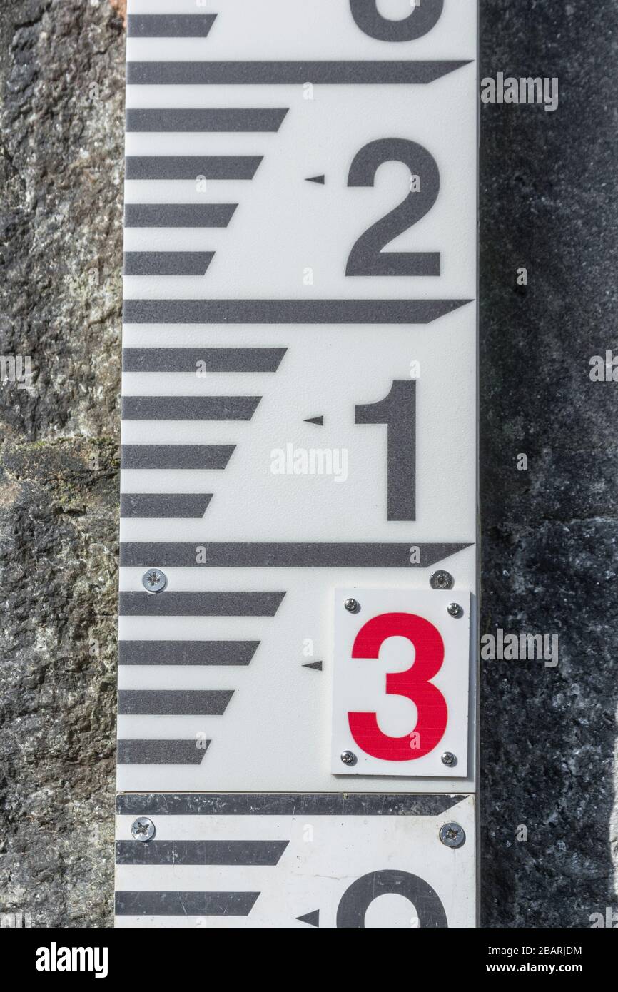 Misuratore del livello dell'acqua del fiume collegato alla parete di sbarramento in pendenza sul fiume Fowey a Lostwithiel. Metafora dell'aumento dei livelli dell'acqua, difese da alluvioni. Foto Stock