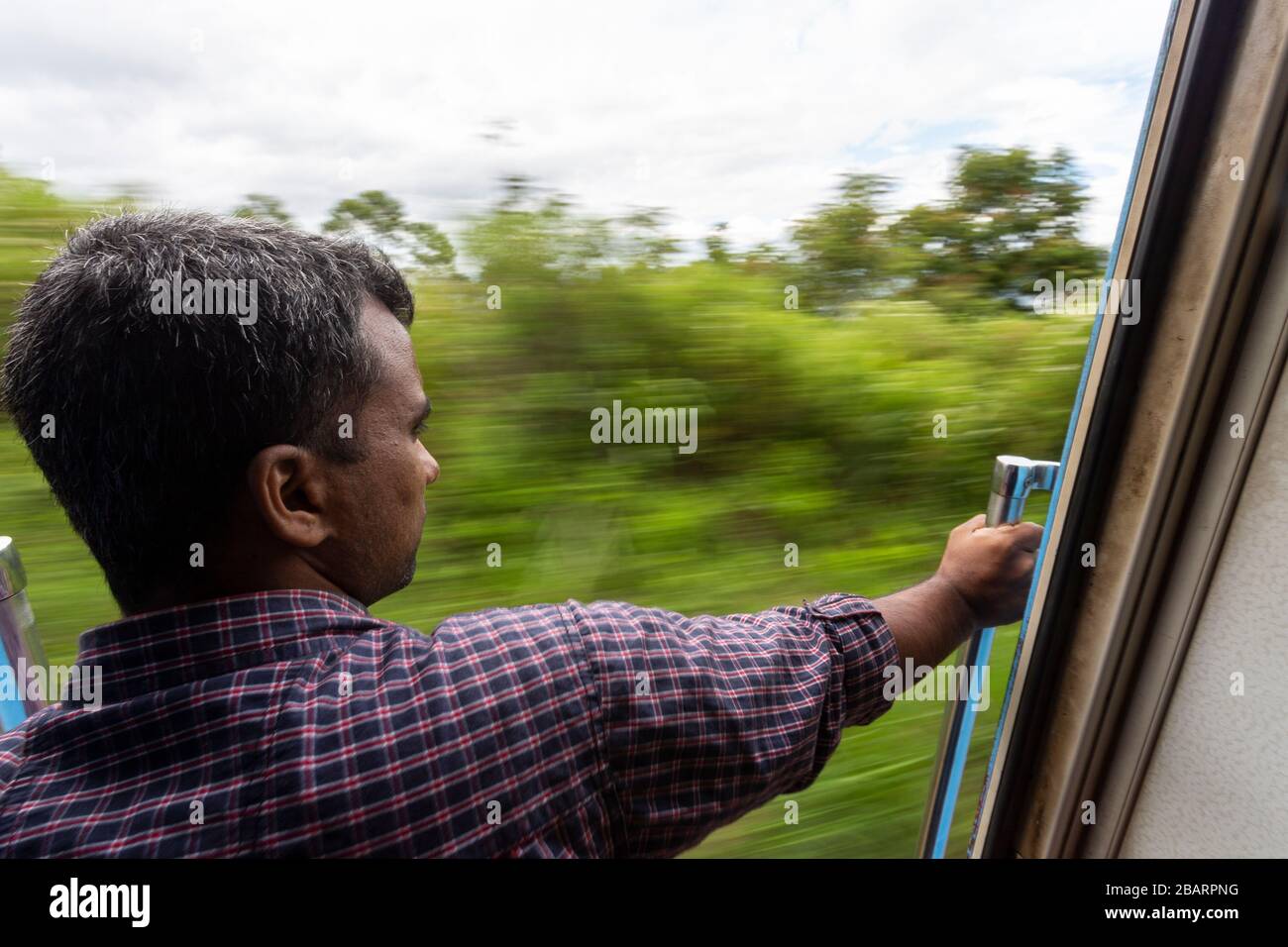 Un uomo locale tiene su una ringhiera all'ingresso di una carrozza ferroviaria aperta nella regione collinare dello Sri Lanka Foto Stock