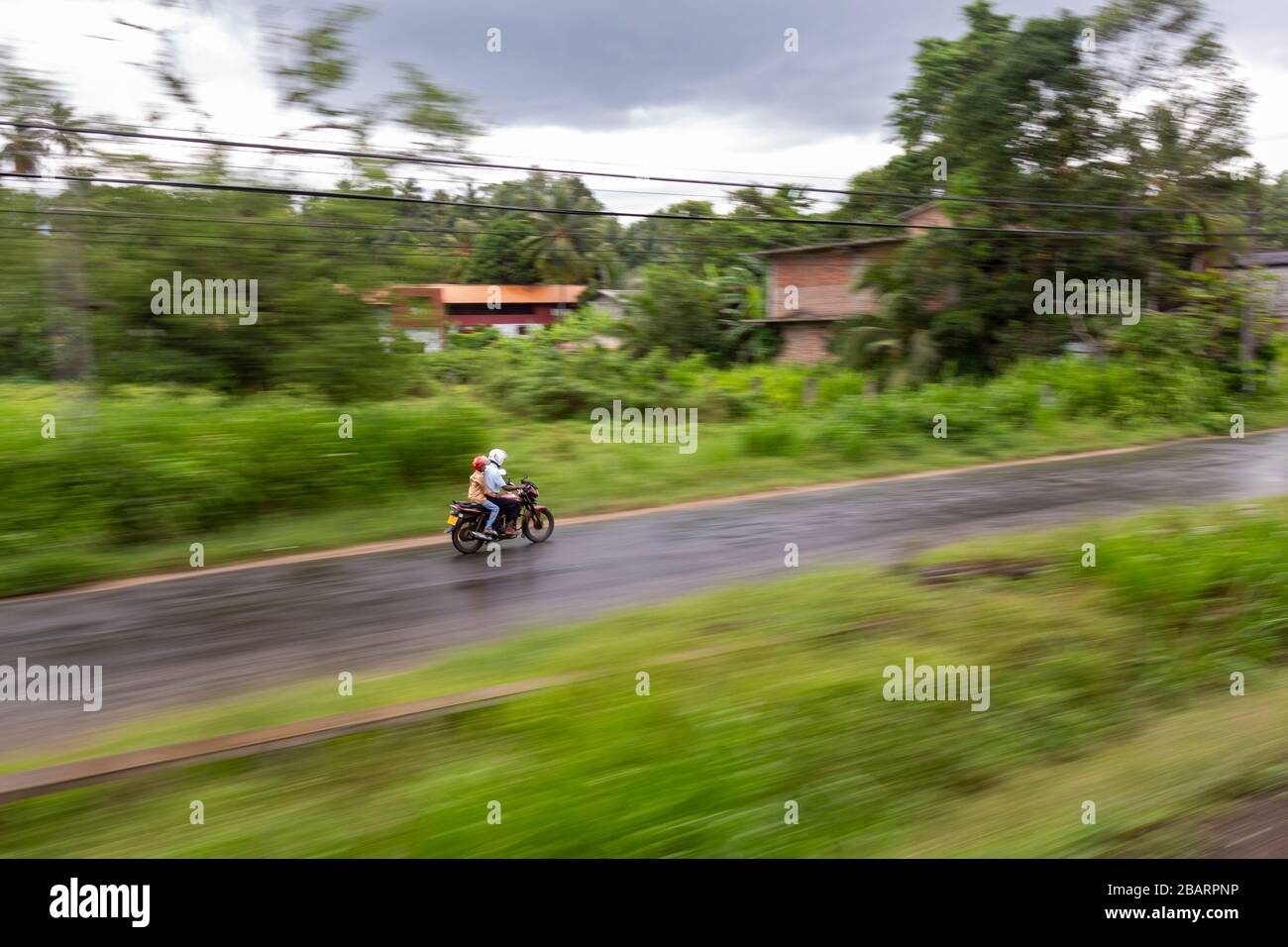 Una coppia locale che viaggia su una moto visto da un treno in movimento nel paese collinare dello Sri Lanka Foto Stock