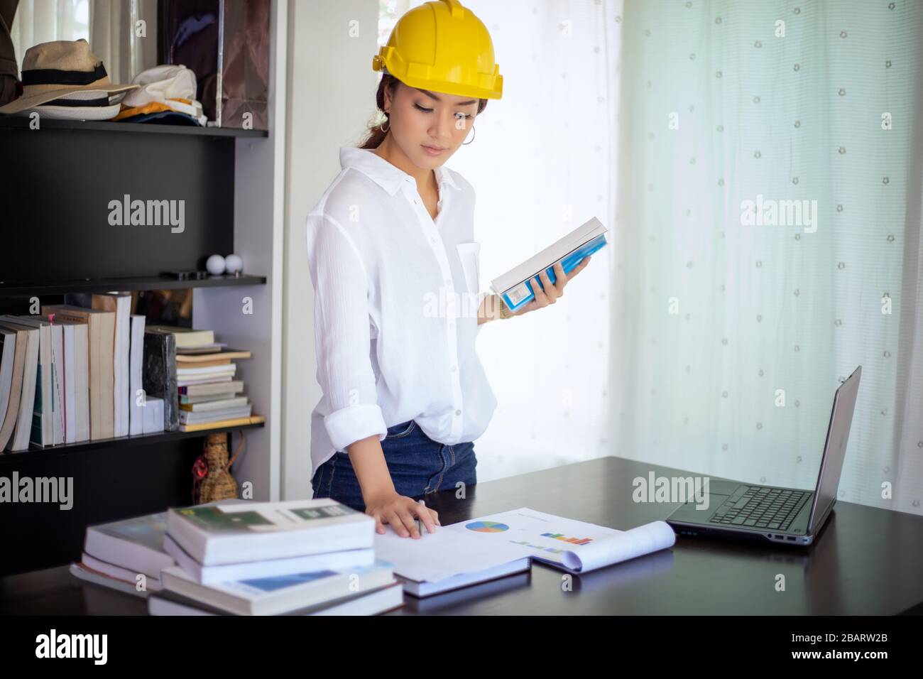 Belle donne asiatiche di ingegneria che controllano il documento e che usano il notebook che lavora da casa per il concetto di distanza sociale e di auto responsabilità Foto Stock