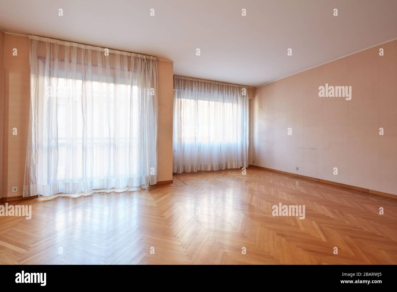 Ampia camera vuota con pavimento in legno e tende bianche all'interno dell'appartamento Foto Stock