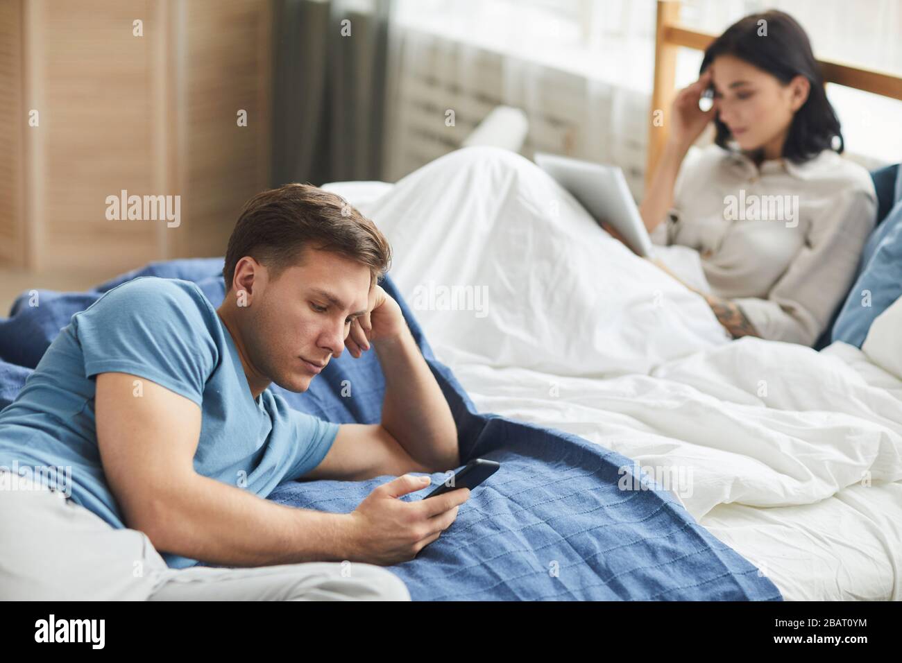 Ritratto di giovane coppia moderna utilizzando dispositivi mobili mentre si siede sul letto, comunicazione problema concetto, copia spazio Foto Stock